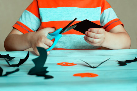 Halloween concept, child cuts out pumpkin and bat figurines from paperの写真素材