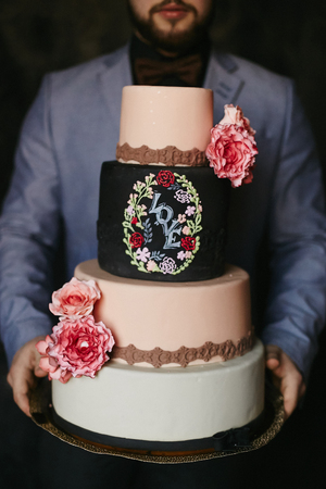Stylish four parts wedding cake with flowers and the lettering love in hands of bearded menの写真素材