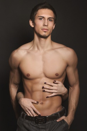 Shirtless, fitness shaped muscular men, with woman's hands on his body, posing at black background.の写真素材