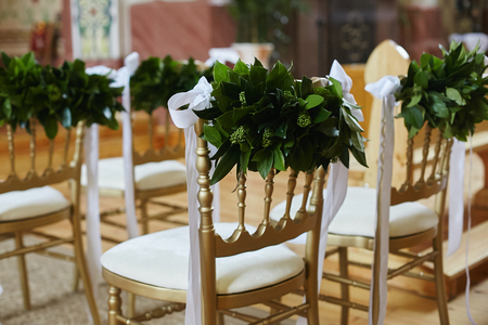 Row of chairs decorated with green leaves and white ribbons for wedding ceremony.の写真素材
