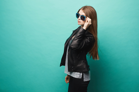 Fashionable model girl, with slim shape, in leather jacket and sunglasses, posing at green background.の写真素材