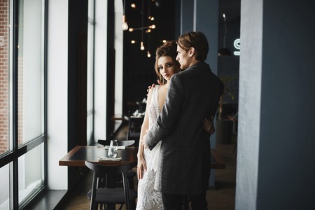 Fashionable and beautiful couple, sexy and elegant brunette model girl with bright make-up and stylish hairstyle in silver dress and stylish handsome men in trendy coat posing at restaurant interior.の写真素材