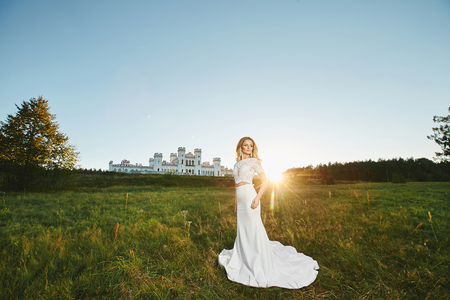 Beautiful blonde model girl with perfect body in fashionable lace dress posing in front of the ancient white castle at the sunsetの写真素材