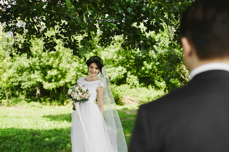Young happy bride with floral wreath in her wedding hairstyle with a bouquet of rose flowers in her hands smiling outdoors in sunny dayの写真素材