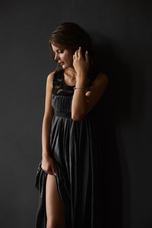 Sexy brunette beauty with perfect body in fashionable evening dress bares her long sexy legs at the dark backgroundの写真素材