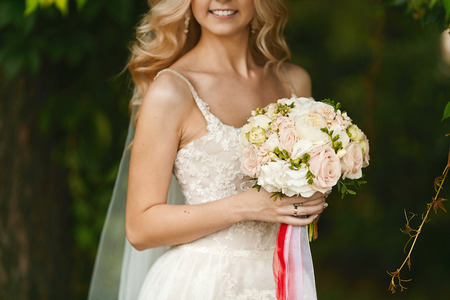 Bouquet of fresh flowers in the hands of a young beauty with blond hair and in the wedding dressの写真素材