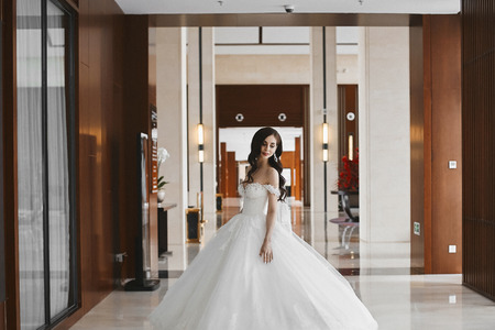 Sexy and young model woman with perfect body and big breasts in the fashionable wedding dress with naked shoulders posing at modern luxury interiorの写真素材