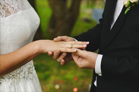 Stylish groom puts on the engagement ring on the finger of his beautiful bride at the wedding ceremony. Strong male hands and beautiful female hands with the wedding ring and elegant manicureの写真素材