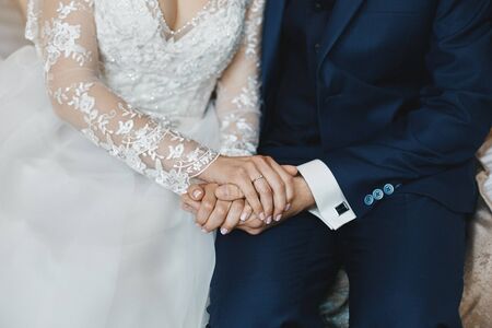 Stylish groom holds the hands of his beautiful bride at the wedding ceremony. Strong male hands and beautiful female hands with the wedding ring and elegant manicureの写真素材