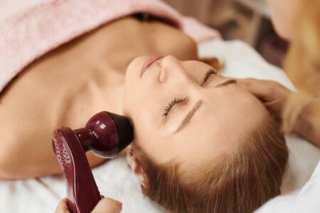 Beauty with perfect face skin on a non-surgical facelifting procedure. Woman receiving electric lift...