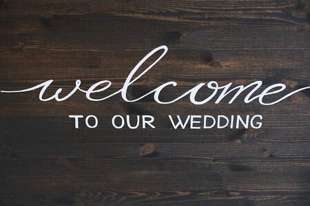 Wooden board with the inscription Welcome to our wedding. White lettering on a dark wooden surface - welcome to our wedding. Greeting inscription on a brown wooden plank - welcome to our wedding.の写真素材