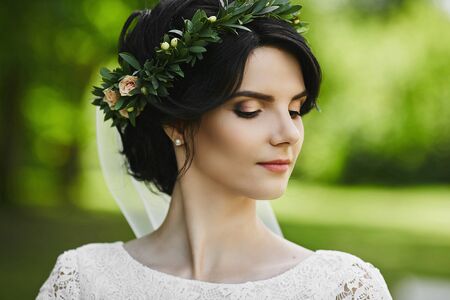 Close-up portrait of a beautiful young bride with floral wreath in her hair posing with closed eyes. Young woman with a wedding hairstyle and bright makeup. Concept of beautyの写真素材