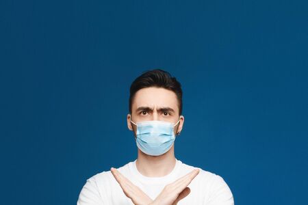 Handsome young man in protective mask against infectious diseases and flu showing gesture enough, isolated at blue background with. Healthcare and health protection conceptの写真素材