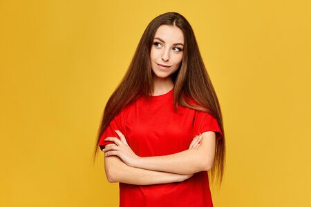 Young female student in a red shirt posing with folded hands at the yellow background, isolatedの写真素材