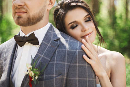 The young bride leans on a stylish groom and stands after the wedding ceremony. A newlywed couple hugging outdoors at natureの写真素材