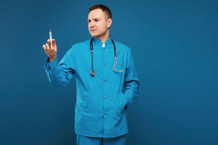 Adult doctor in blue medical uniform holding a medical syringe for injection, isolated on blue...