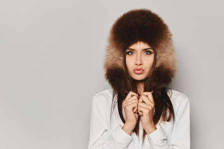 Fashionable model girl with gentle makeup in the black skirt, white blouse and blue fur mittens posing at the grey background, isolated.の写真素材