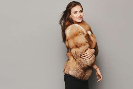 Side view of a model girl in an expensive luxurious fur coat isolated at the grey background. Winter...