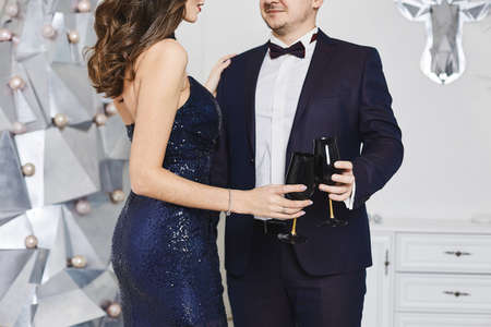 Man in stylish suit and sexy model girl with perfect body in evening dress posing on Christmas eve