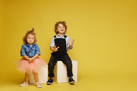 Cute children posing over a yellow background. Sad little girl and happy boy in casual outfits on the yellow background, isolated with copy spaceの写真素材