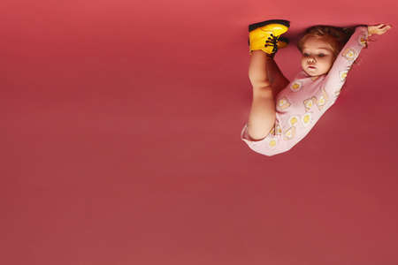 A cute little child girl in bright yellow boots stands on the head over the pink background, isolated. Kids fashionの写真素材