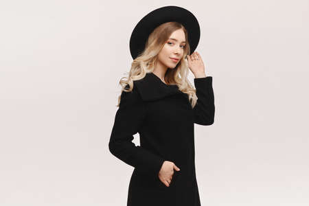 Young model woman in a black coat and black stylish hat posing over white background, isolated with copy space for text or productの写真素材
