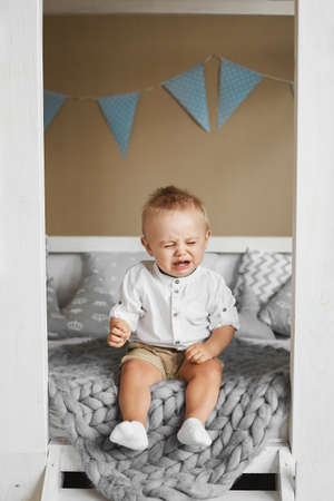 Little boy crying while sitting on the bedの写真素材