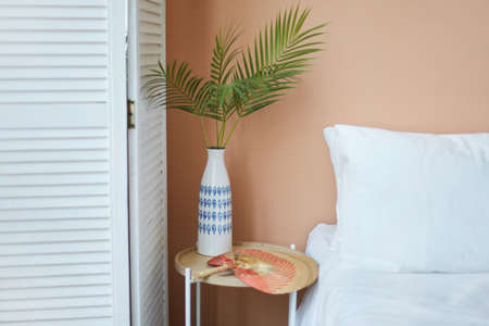 Cozy interior of the white retro wardrobe, white bed and wooden table and white vase on it with...