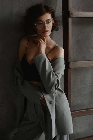 Seductive model woman with perfect figure and full lips wearing a black cami top and eyewear posing near the grey wallの写真素材