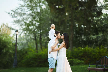 Happy young family, a beautiful young woman with a handsome man and adorable toddler boy, young mother her husband and their little son, posing at a city park on a warm summer dayの写真素材