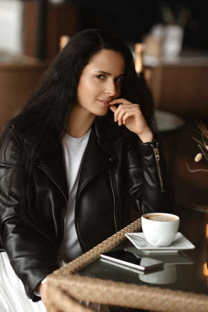Cute European female model sitting at the table in a cafe and looking at the camera