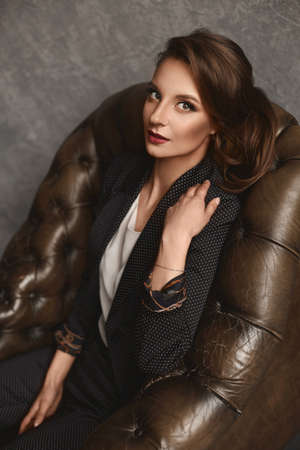 Close up fashion portrait of a young woman with perfect makeup and hairdo in a trendy suit and...