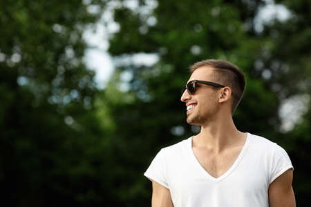 Happy guy in sunglasses posing on a summer day. A handsome young man with a broad smile and snow-white teeth posing outdoors in a casual outfitの写真素材