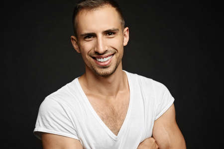 Happy guy in white t-shirt isolated at dark background. A handsome young man with a broad smile and...