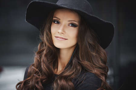 Closeup fashion portrait of a young model woman with trendy makeup wearing black fashionable hat posing outdoorsの写真素材