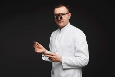 Caucasian male doctor in binocular loupes glasses and with surgeon equipment at the black...