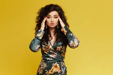 Beauty fashion model girl in a trendy dress, with bright makeup, amazed young brunette woman isolated on yellow background, posingの写真素材