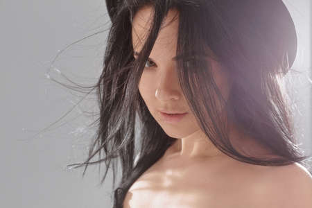 Fashion portrait of a model girl with nude makeup and fluttering perfect black hair wearing a trendy black hatの写真素材