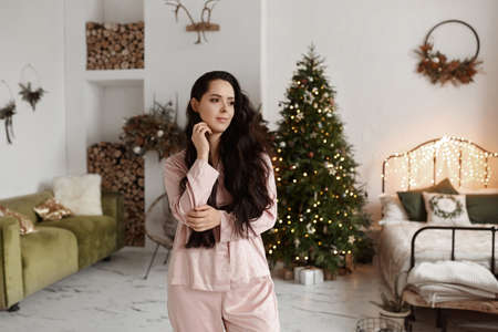 Pretty model girl with dark hair wearing modish sleepwear posing in decorated for Christmasの写真素材