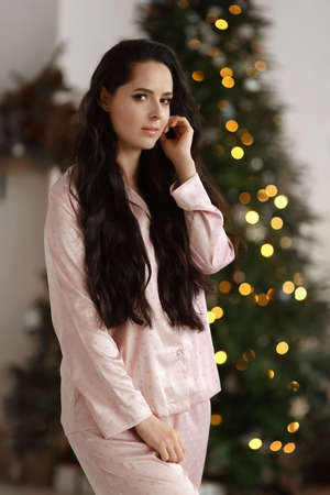 Pretty young woman with dark hair wearing modish sleepwear posing near decorated Christmas treeの写真素材