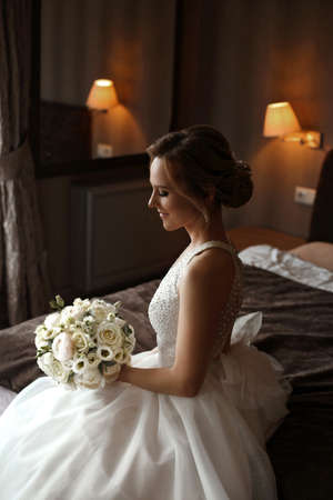 Portrait of a happy charming bride in stylish wedding dress posing with a bridal bouquet in the interiorの写真素材