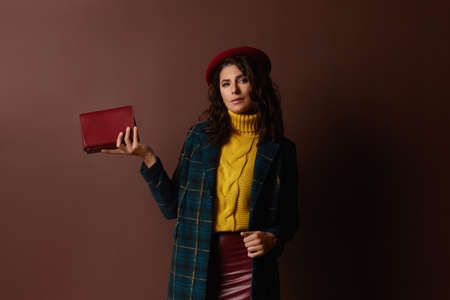 Fashion portrait of a charming woman in a trendy hat, fashionable coat and skirt keeping classic...