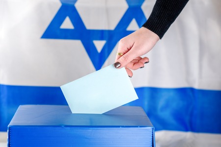 Israeli Young woman putting a ballot in a ballot box on election day. Close up of hand with white votes paper on Israel flag background. Mockup, space for text.の写真素材