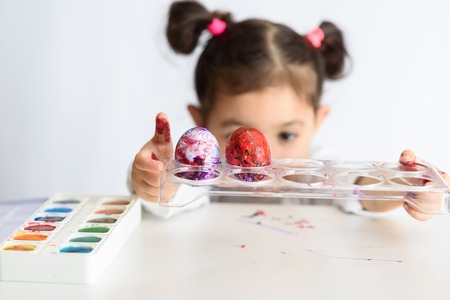 Happy easter. Funny little girl painting Easter eggs. Happy toddler preparing for Easter.の写真素材