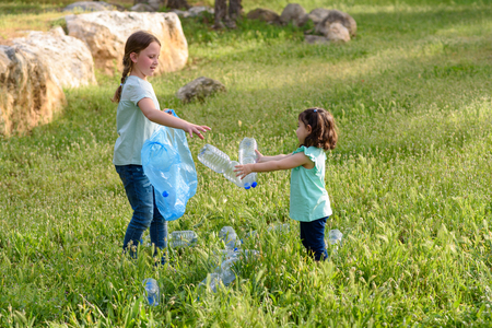 Cute little girls cleaning up plastic litter on grass. Children Volunteers cleaning up litter and putting plastic bottle into recycling bag.の写真素材