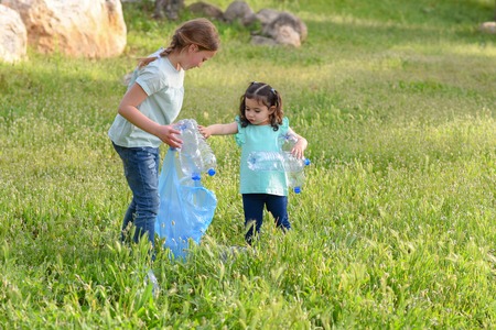Cute little girls cleaning up plastic litter on grass. Children Volunteers cleaning up litter and putting plastic bottle into recycling bag.の写真素材