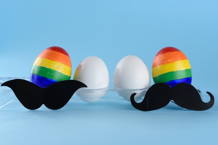 Lgbt family. Parents eggs man with lgbt flag color and two white baby eggs on blue background. Creative idea for illustration surrogacy law, right homosexual couple adoption and raising a child.の写真素材