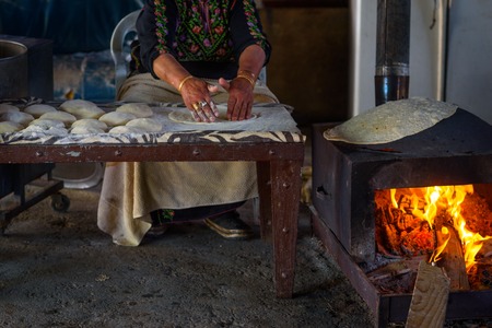 Old arab woman cooking traditional bedouin cuisine food - taboon bread or flatbread. Close up of...