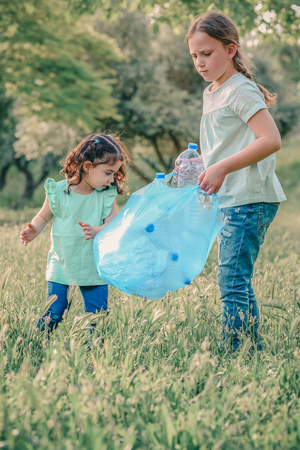 Little girls takings plastic bottles from grass. Children picking up litter in the forest .の写真素材