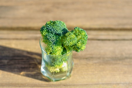 Healthy Green Organic Raw Broccoli Florets Ready for Cooking. Bunch of fresh green broccoli in glass on wooden table close up on the background of a stone wall.の写真素材